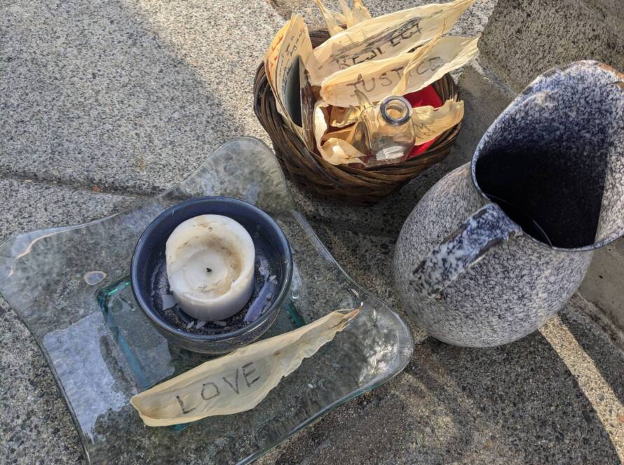 a chalice with unlit candle, a water pitcher, and a basket with dried corn leaves with writing. Words are "Love", "Respect", and "justice".