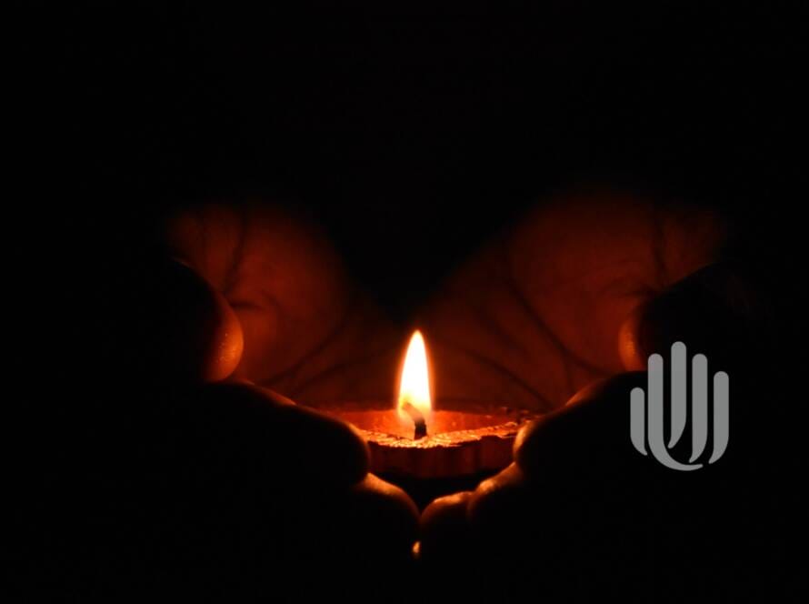 hands in darkness cupping a single candle flame illuminating the palms.