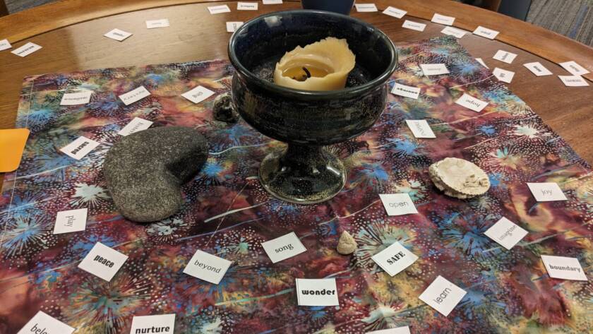 centrepiece with a chalice, stones, shells, and words. Words read wonder, grace, hope, learn, safe, sing, seek, nurture, beloved, peace, play, sacred, inspire, courage, open, etc.