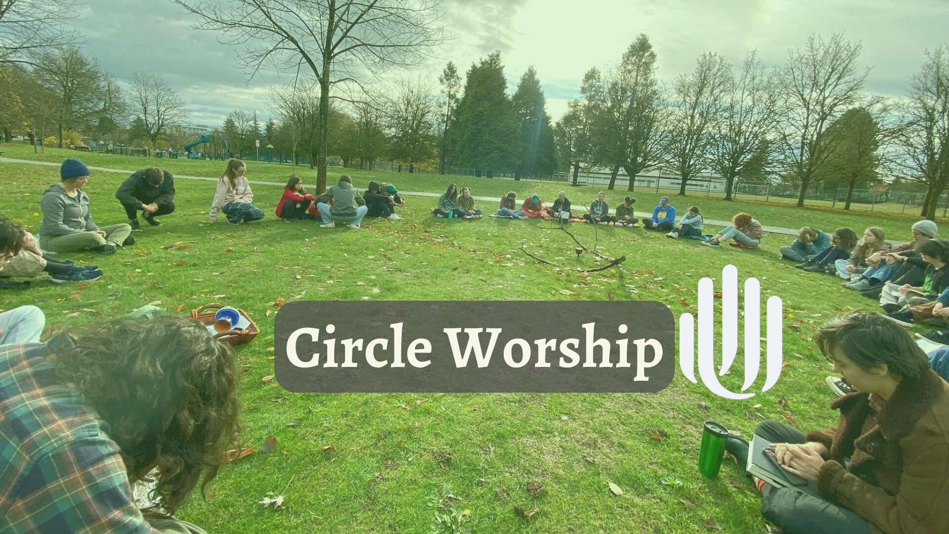 A circle of people sitting on the grass in a park with a chalice lit in the centre. Text reads "Circle Worship"