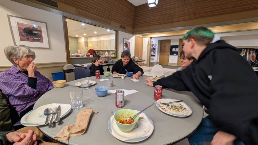 children, adults, and elders eat together and read questions from cards in the centre of the table