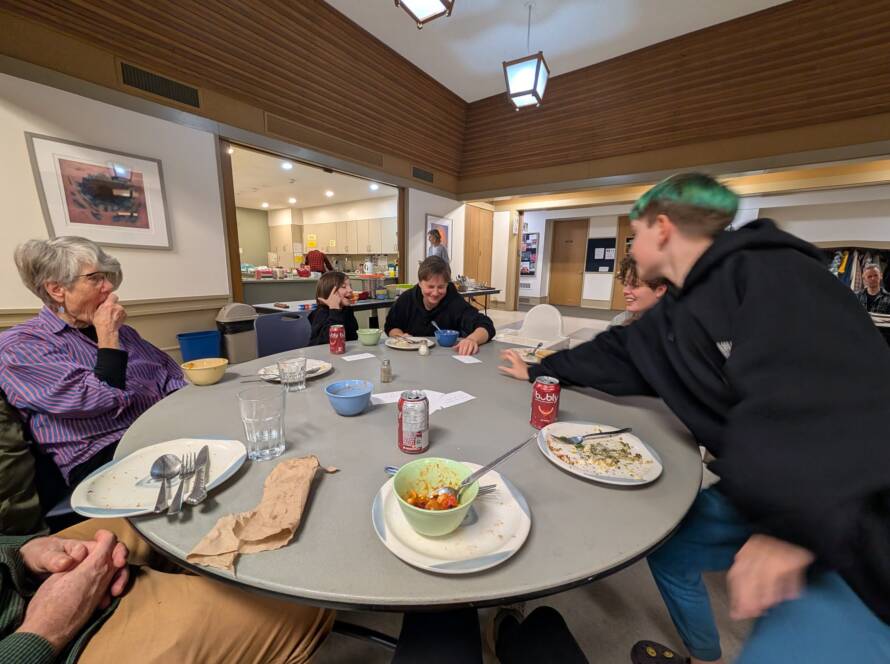 children, adults, and elders eat together and read questions from cards in the centre of the table